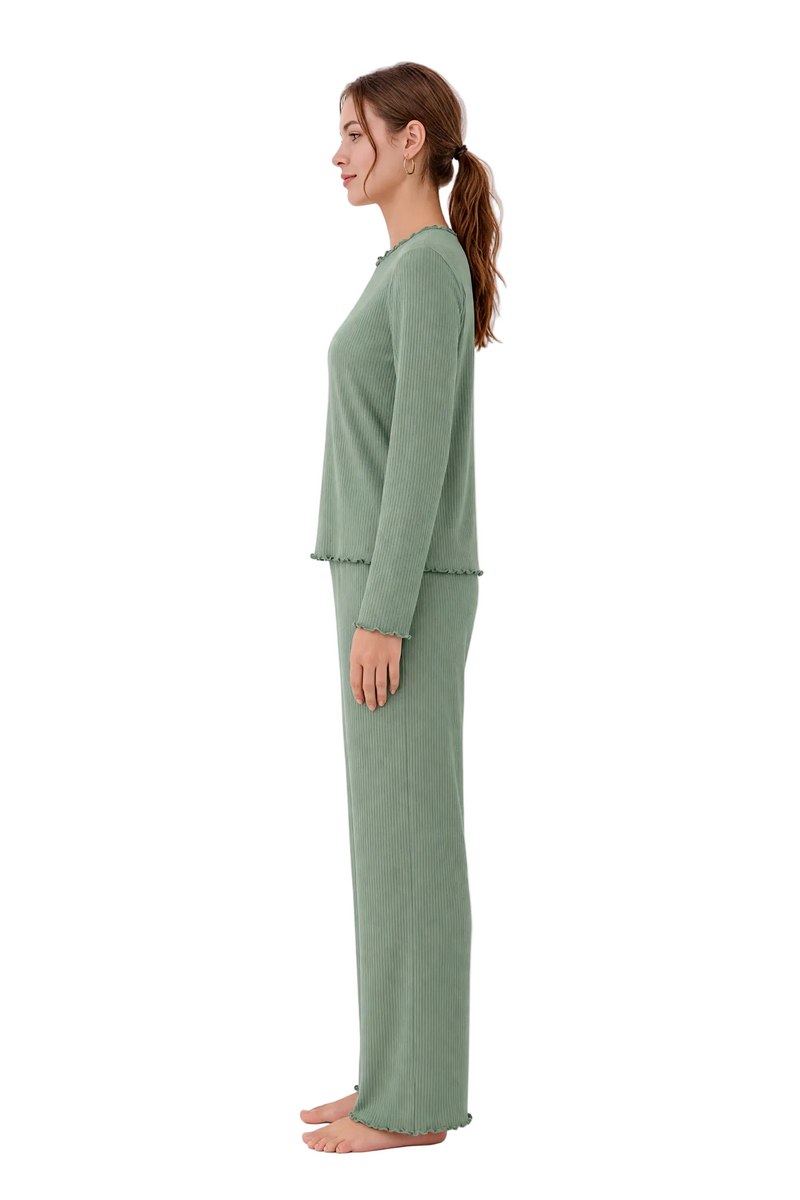 A woman stands in profile wearing a matching sage green knit loungewear set with a long-sleeve top and wide-leg pants, photographed against a plain white studio background.